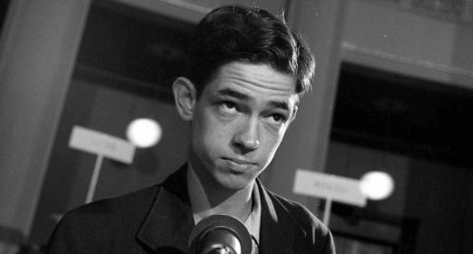 A man in a suit speaking about himself into a microphone.