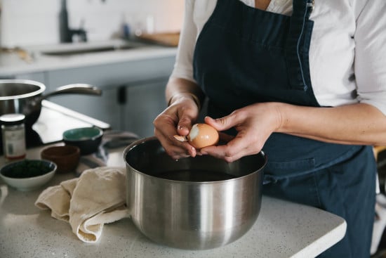 Chef Sarah is peeling soft boiled egg in kitchen. 