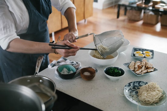 Chef Sarah is pouring noodles into chicken broth. 