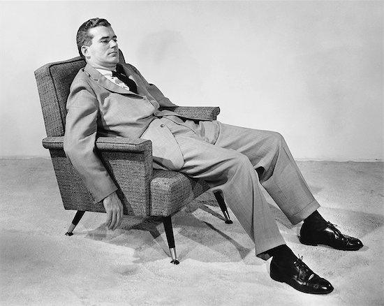 A manliness in a suit sitting in a chair.