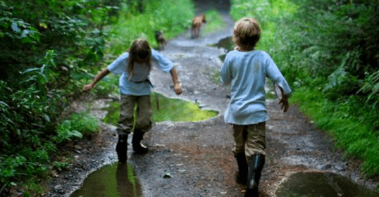 Two children running down a muddy path in the woods, establishing their connection with nature.