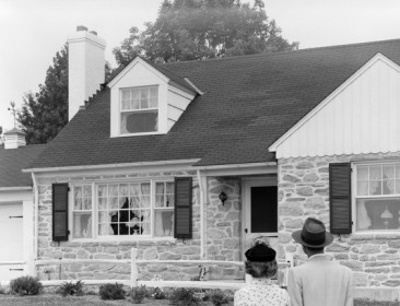 Black and white photo of a couple standing in front of a house ready to sell.