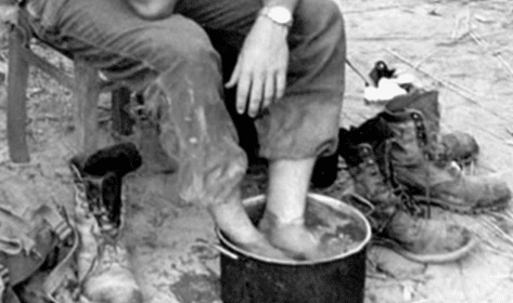 A man sitting on a chair with his feet in a bucket is giving his feet some care.