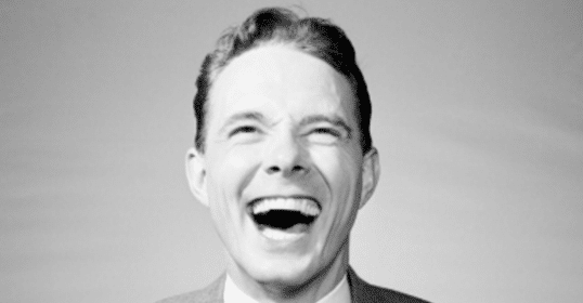 A black and white photo of a man laughing, captured in 1928.