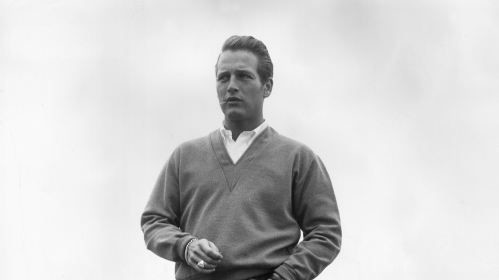 A man in a sweater and khakis standing on a dock.