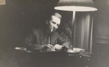 An old photograph of a man sitting at a desk with a lamp while working.