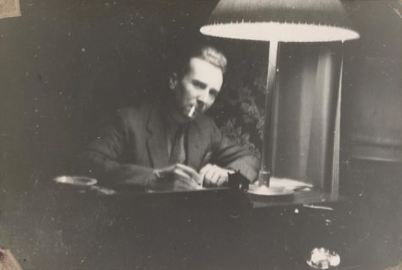 An old photograph of a man sitting at a desk with a lamp while working.