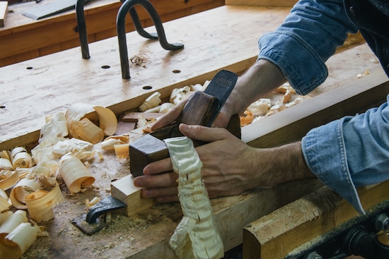 Man craftsman using hand plane on wood.