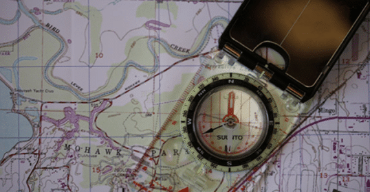 A compass rests atop a map, aiding in manual land navigation.