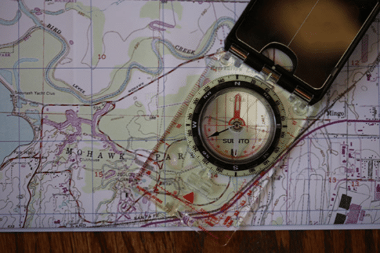 A compass rests atop a map, aiding in manual land navigation.