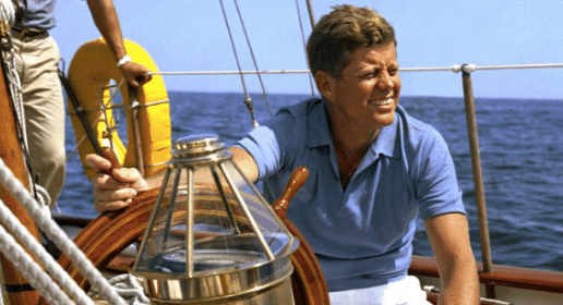 John F. Kennedy on a sailboat, showcasing summer style in a casual dress.