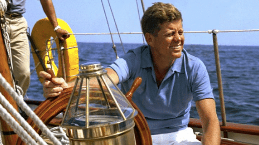 John F. Kennedy on a sailboat, showcasing summer style in a casual dress.