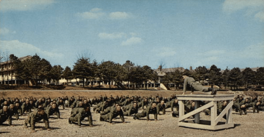 A group of men standing on a wooden platform during a *PT test*.
