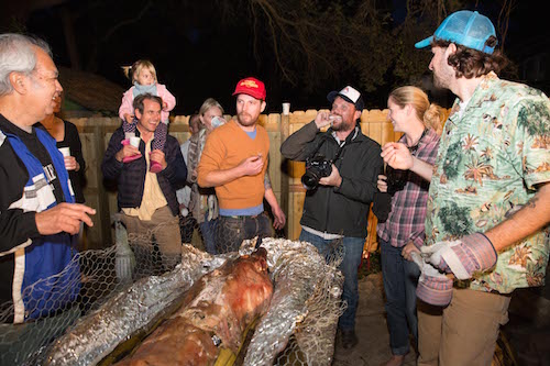  homens curtindo festa noturna com porco assado.