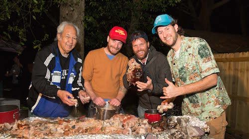 A group of men cooking pig Hawaiian style around a large barbecue.