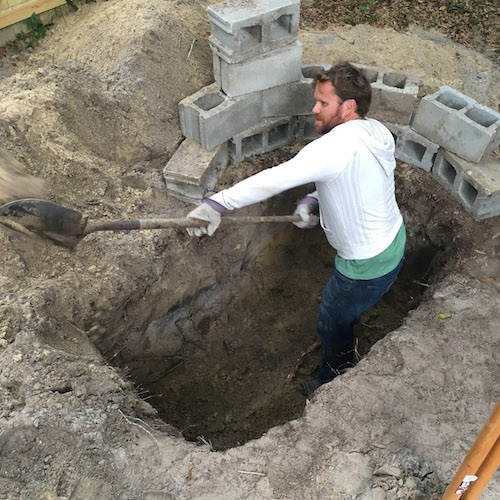 um homem cavando uma sepultura de forma quadrada com blocos.