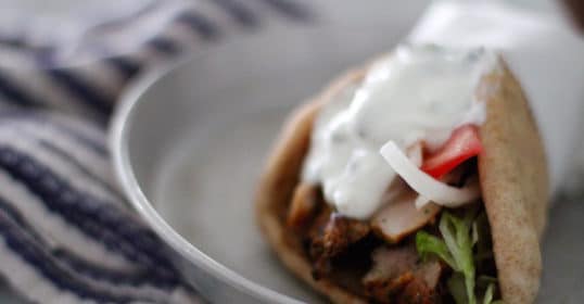 An authentic Greek plate with gyro meat and vegetables on a pita.