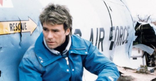 A man in a blue jacket expertly leaning against a plane, showcasing his urban survival skills.