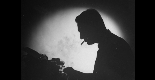 A silhouette of a man typing on a typewriter under the moonlight.