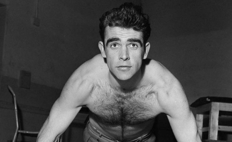 A shirtless man breaking through a plateau in a gym while doing push-ups.