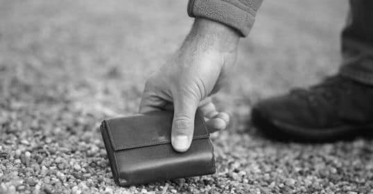 A man putting a wallet on the ground in a black and white photo.