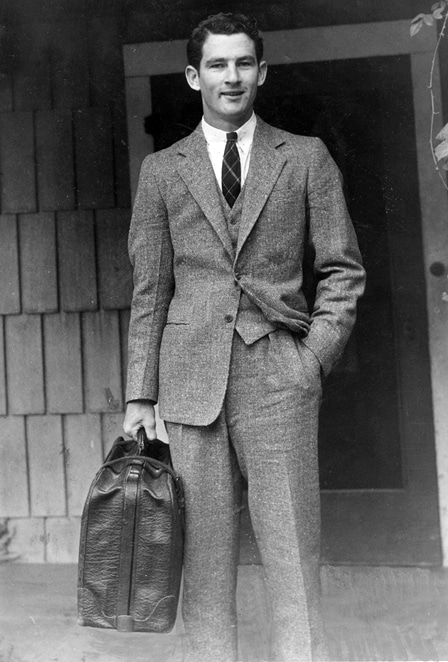 A man in a suit packing a suitcase for a one-week business trip.