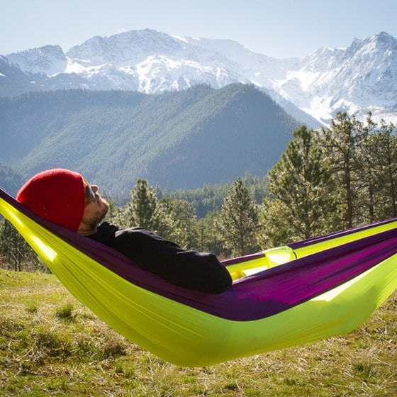 Man napping relaxing on hammock with mountains in background.