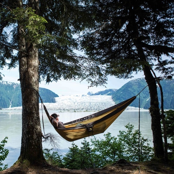 Man relaxing napping in hammock with glacier in background.