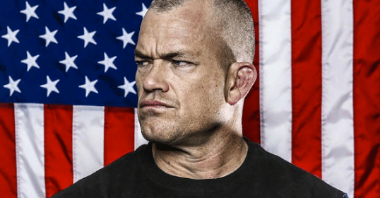 Jocko willink navy seal side posing having american flag as background.