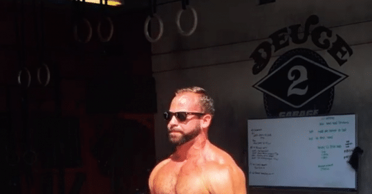 A man holding a barbell in front of a gym after a workout.