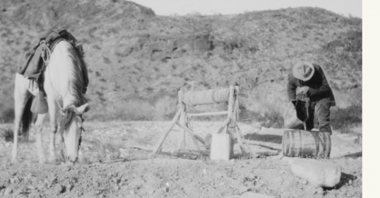 A man stands next to a horse in the desert, embodying a mythic scene of scarcity.