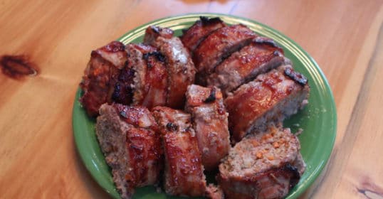 Bacon-wrapped meatloaf on a green plate on a wooden table.
