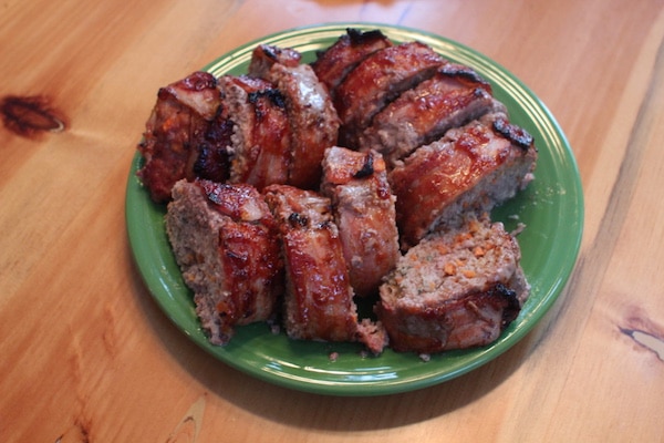 Bacon-wrapped meatloaf on a green plate on a wooden table.