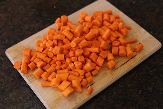 Raw chopped carrots on wooden cutting board.