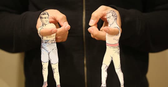 A man's hands holding two vintage paper cut outs of a man and a woman.