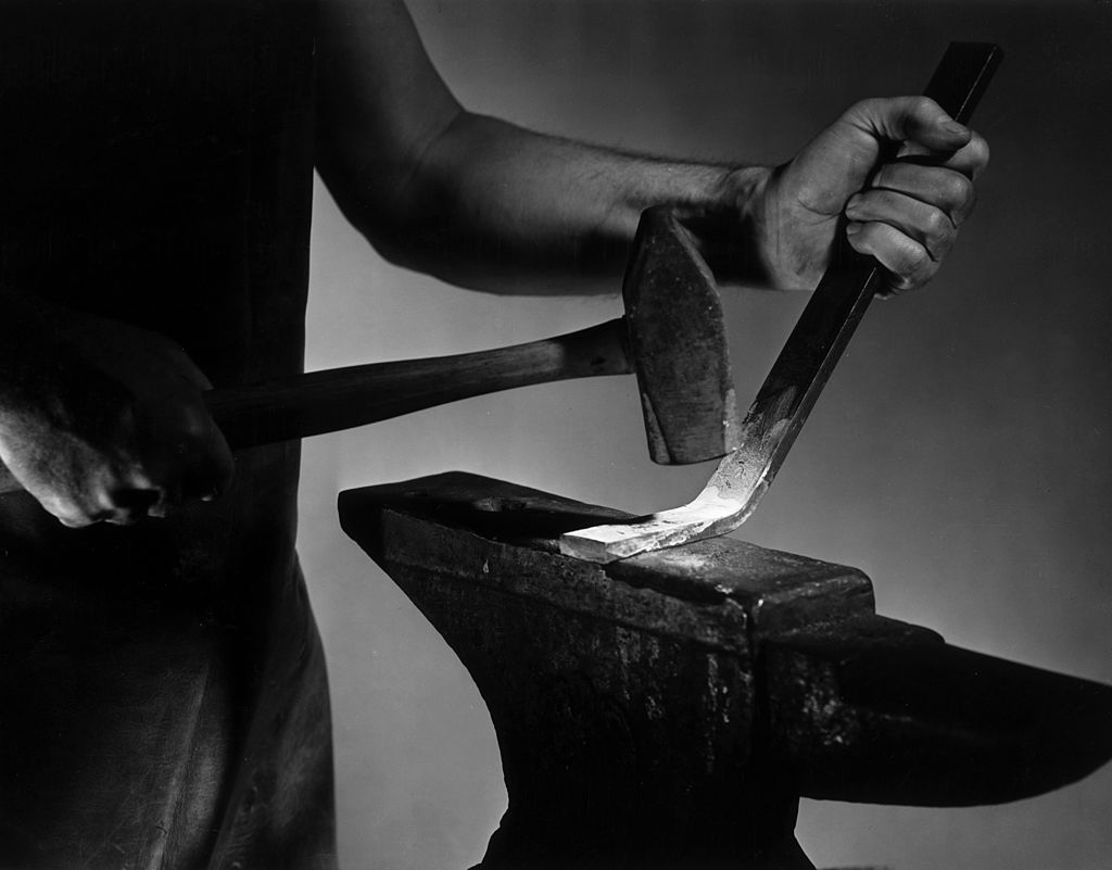 A blacksmith tirelessly hammering a piece of metal on an anvil.
