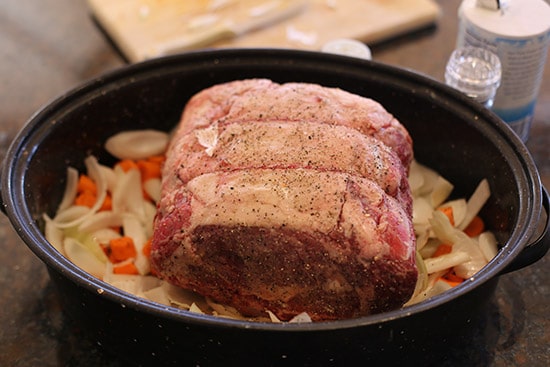 Prime rib roast in roasting pan on vegetable bed.