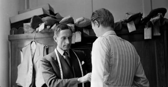 A man in a suit is helping another man find a good tailor.