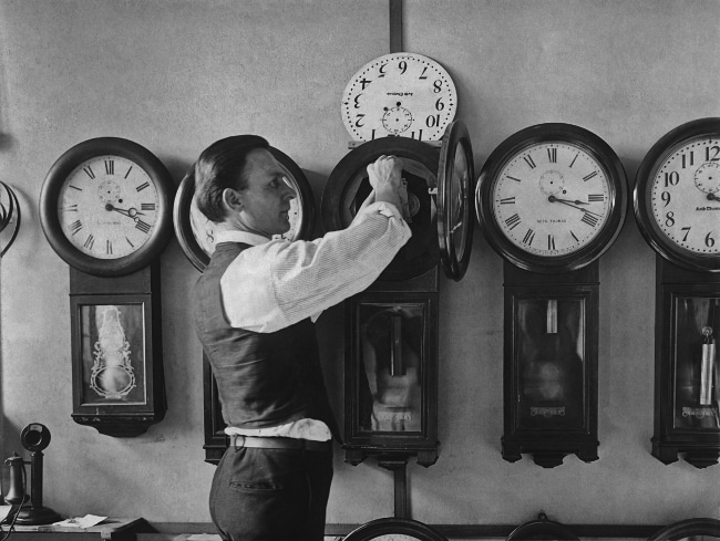 A man is tracking time by putting clocks on a wall.