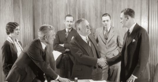 How to get a job promotion: A group of business people shaking hands in an office.