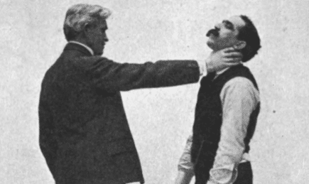 In this vintage photo, a man in a suit is seen touching another man's neck during a Jiu-Jitsu lesson.