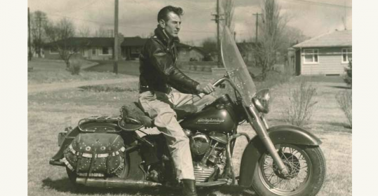 An old photo of a man on a motorcycle wearing leather.