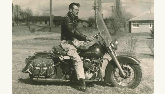 An old photo of a man on a motorcycle wearing leather.
