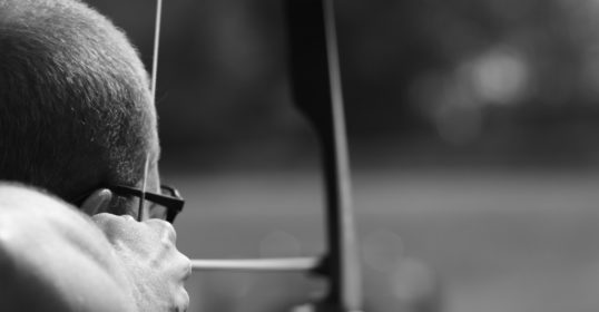 The man with glasses is focused on aiming at the archery target, embodying the essence of precision.