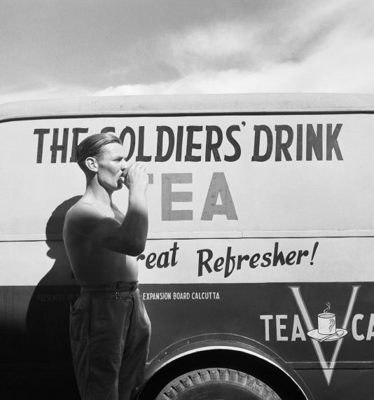 Vintage british soldier drinking tea next to van.