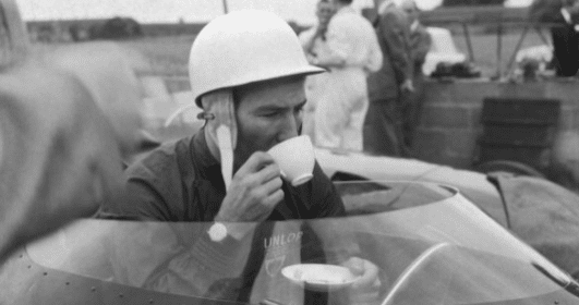 A man in a helmet sipping tea from a cup in a race car, honoring a manly tradition.