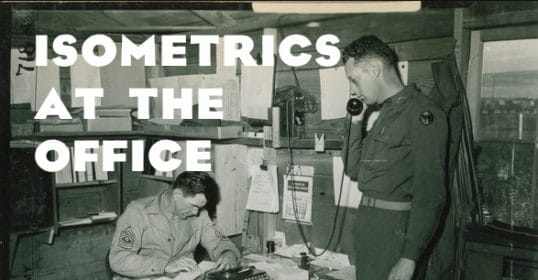 A man in uniform is working at an office desk with another man in uniform.