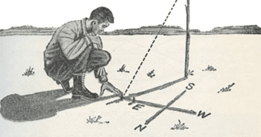 A man kneels on the ground with a compass in his hand, focusing on finding his direction.