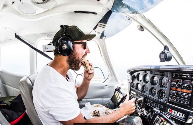 Pilot in small airplane eating bbq sandwich.