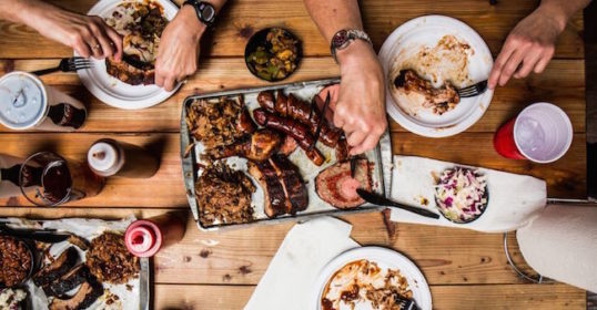 A group of people enjoying BBQ on a wooden table.